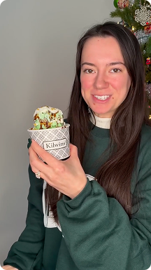 Woman holding dubai chocolate ice cream sundae in front of a christmas tree